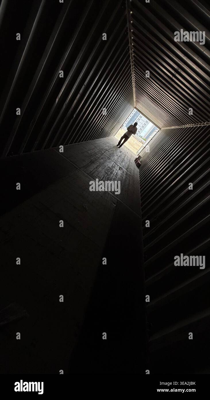 Die Silhouette eines Mannes, der durch einen dunklen Welltunnel in Richtung helles Licht geht und eine dramatische Perspektive und führende Linien schafft. - Smartphone-aufgenommenes Stockfoto