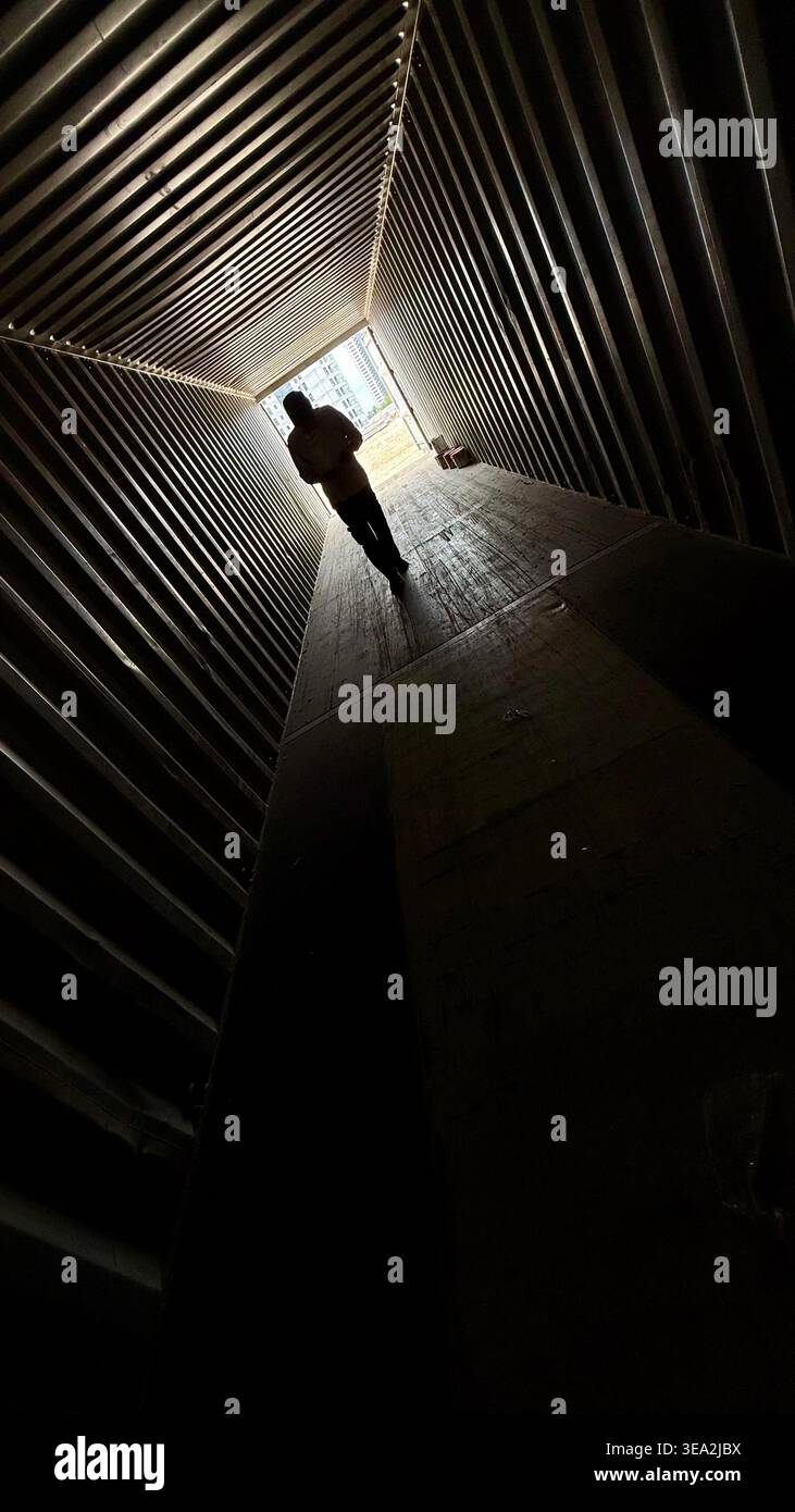 Die Silhouette eines Mannes, der durch einen dunklen Welltunnel in Richtung helles Licht geht und eine dramatische Perspektive und führende Linien schafft. - Smartphone-aufgenommenes Stockfoto