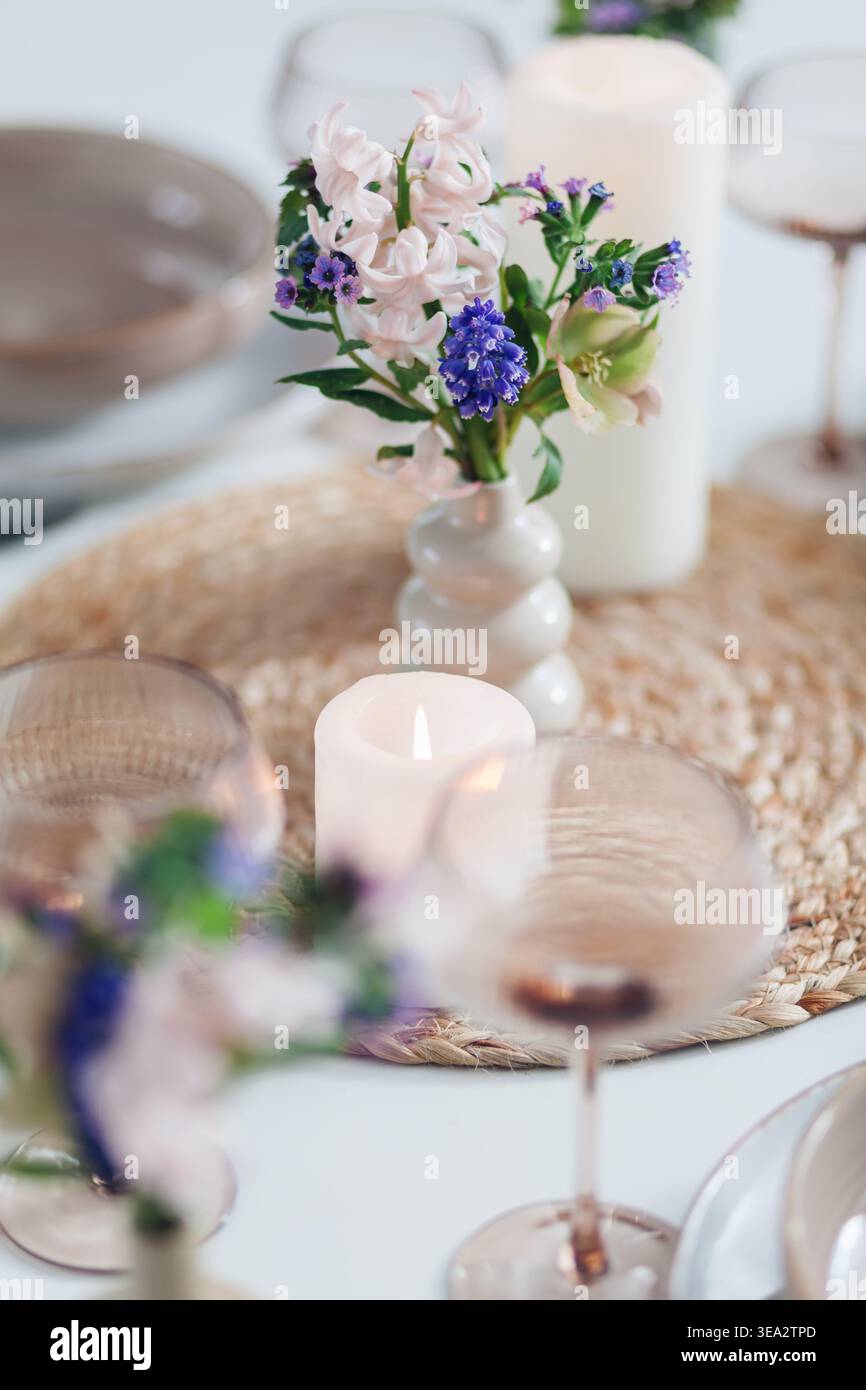 Tisch dekoriert mit Frühlingsblumen in Vasen und Kerzen für das Abendessen zu Hause. Nahaufnahme des Blumenstraußes nach Geschirr, Besteck Stockfoto