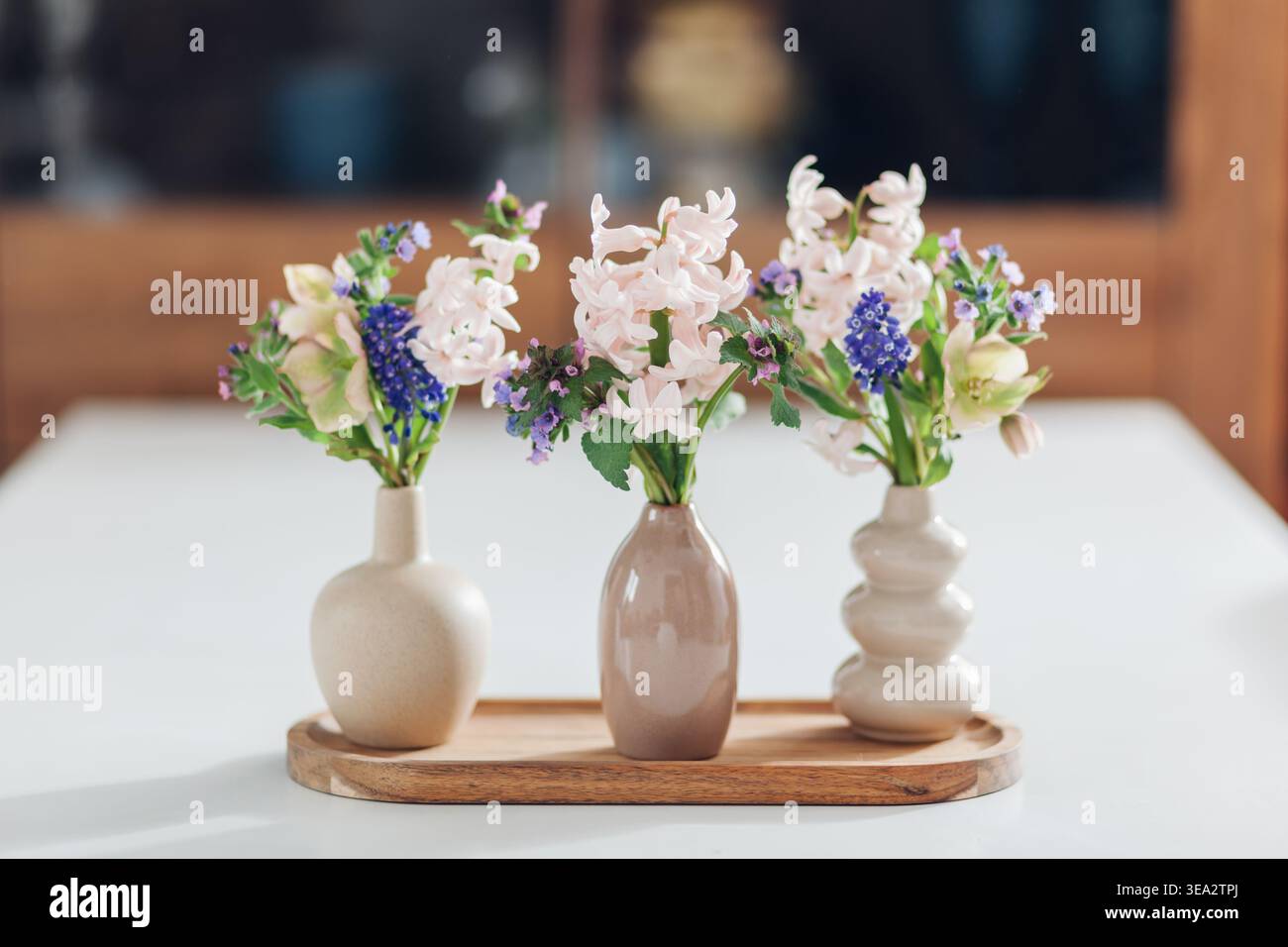 Tisch mit Frühlingsblumen in Vasen auf Holztablett zu Hause dekoriert. Nahaufnahme von drei kleinen Blumenstraußen, die von einem Schrank aufgestellt wurden Stockfoto