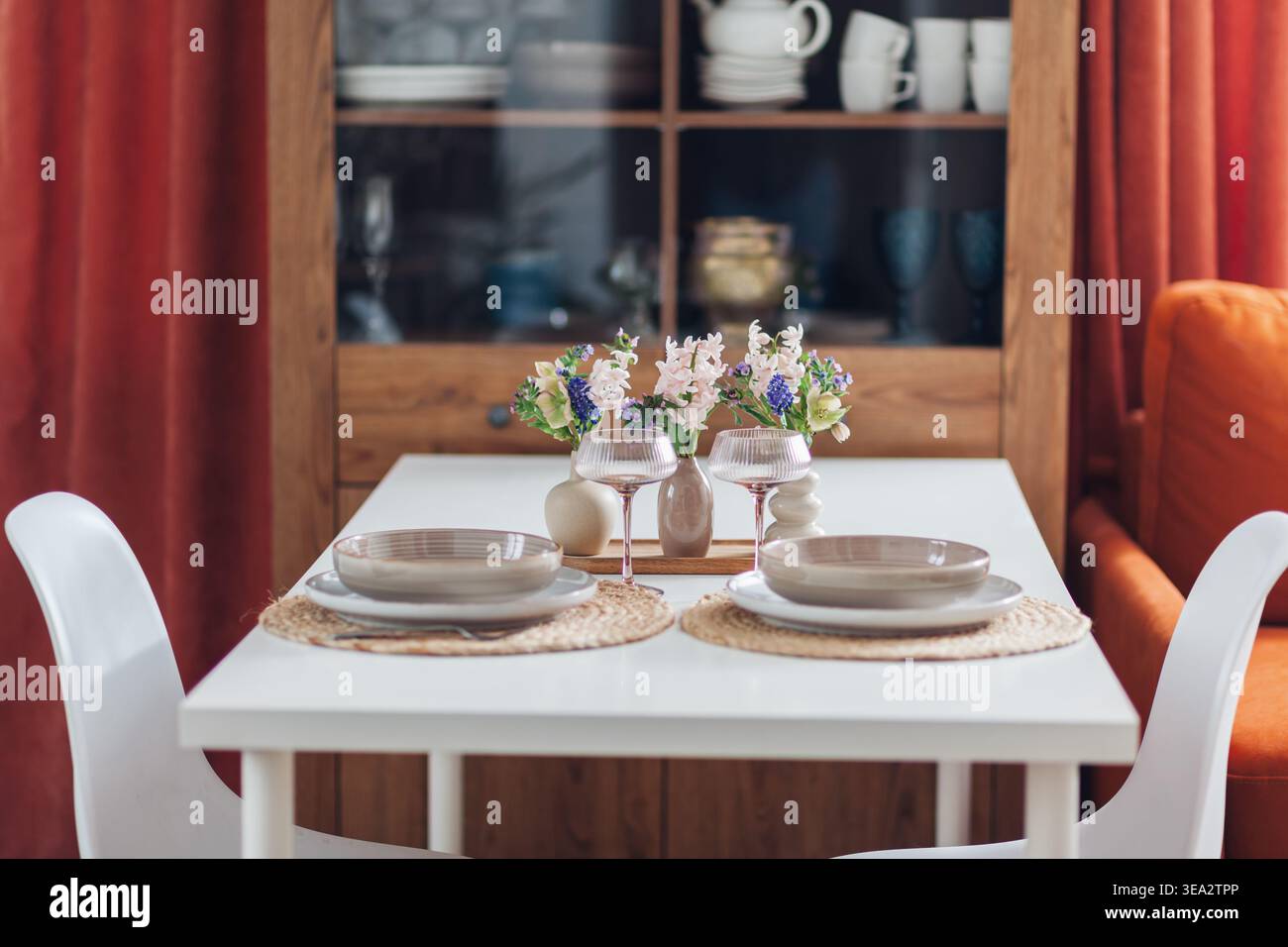 Tisch für zwei Personen, dekoriert mit Frühlingsblumen zum Abendessen zu Hause, in einem Schrank mit Geschirr, Besteck und Couch Stockfoto
