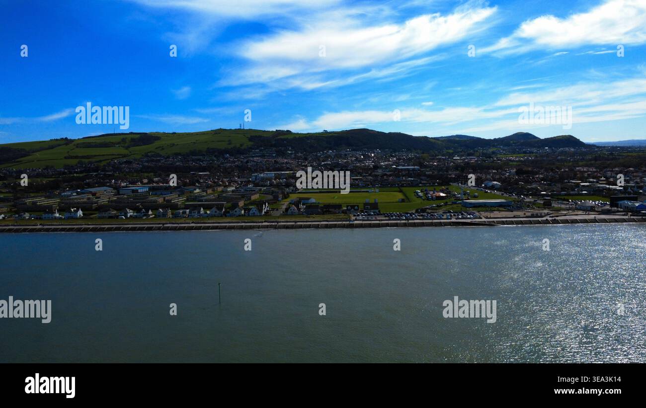 Aus der Vogelperspektive auf die Küstenstadt Prestatyn mit der Küste, den städtischen Gebäuden und den sanften grünen Hügeln unter dem hellblauen Himmel Prestatyn, Wales Stockfoto