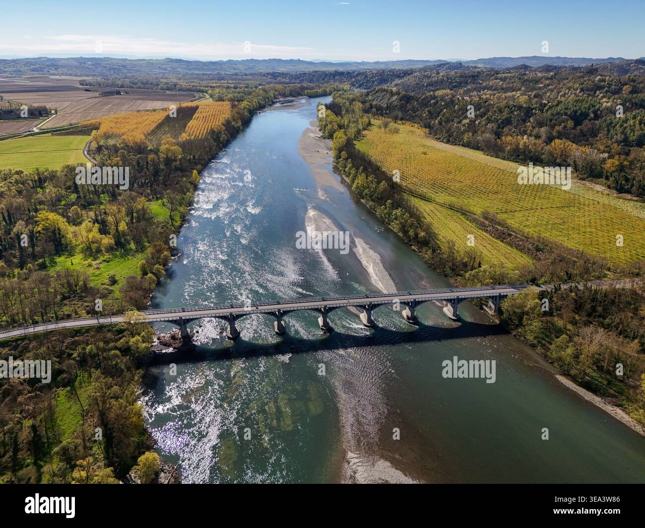 Aus der Vogelperspektive auf den Parco Fluviale del Po und den Po Fluss mit einer bogenförmigen Brücke über das Wasser, üppigen grünen Ufern und sanften Hügeln unter klarem Himmel Stockfoto