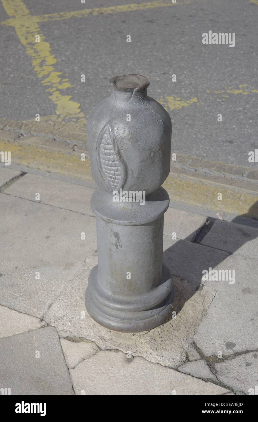 Gusseiserner Granatapfelspoller, Symbol von Granada, auf einem gerissenen Steinpflaster neben einer Straße mit gelben Markierungen, Andalusien, Spanien. Stockfoto