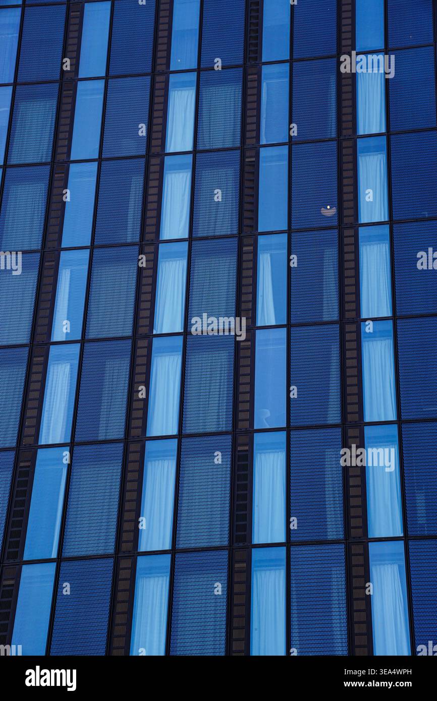 Moderne Glasfassade mit blau getönten Fenstern und Vorhängen im Inneren, die sich wiederholende geometrische Muster in der städtischen Umgebung Wiens bilden Stockfoto