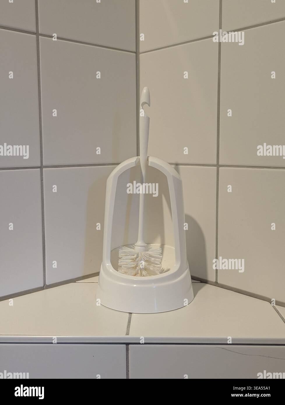 Ein minimalistisches weißes Toilettenbürstenset, das auf einer gefliesten Oberfläche in einer Badezimmerecke steht. Sauberes und funktionales Design für die Haushygiene und die Hausreinigung Stockfoto