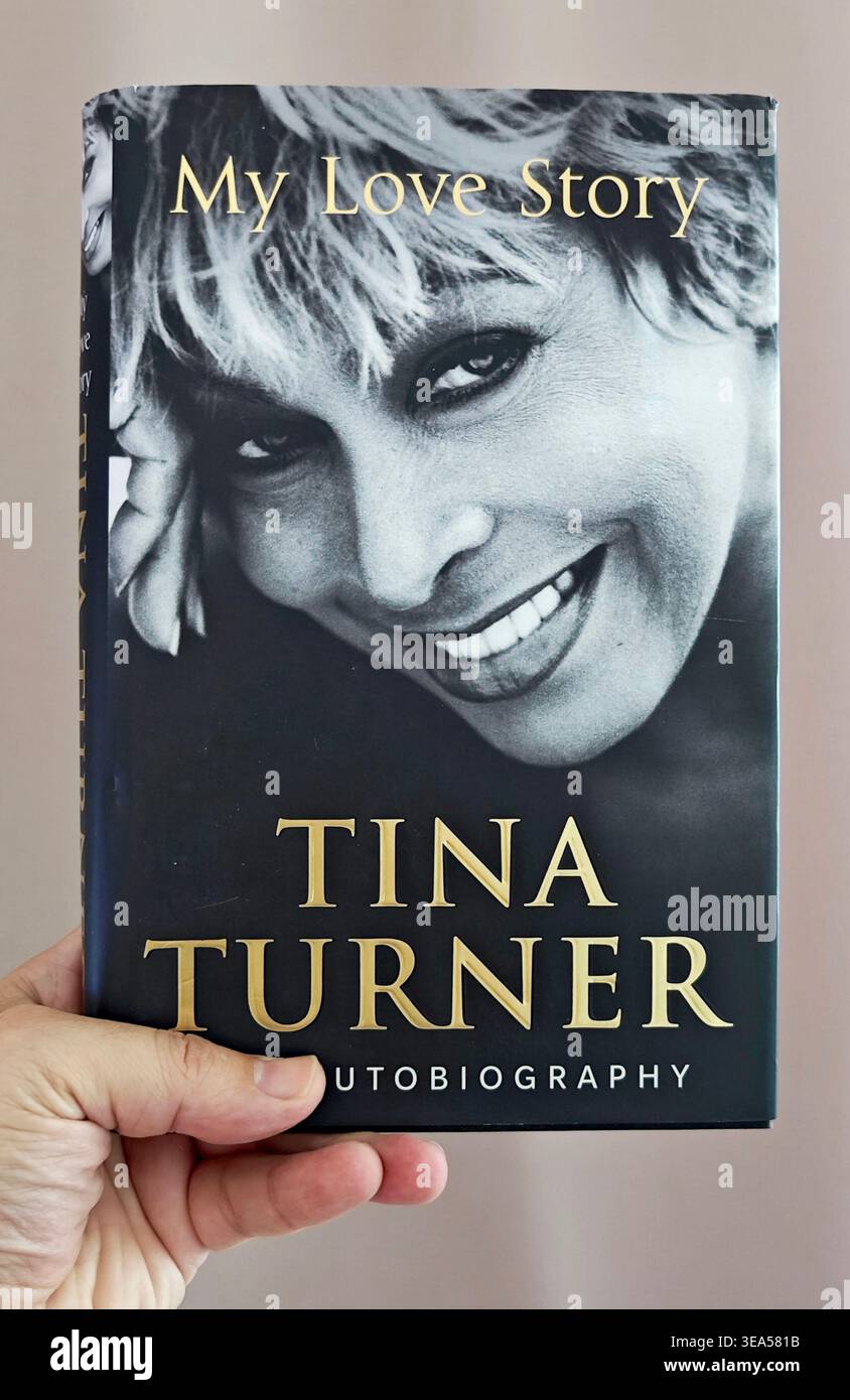 Hand hält das Autobiographiebuch „My Love Story“ von Tina Turner mit einem schwarz-weißen Nahporträt des lächelnden legendären Rocksängers Stockfoto