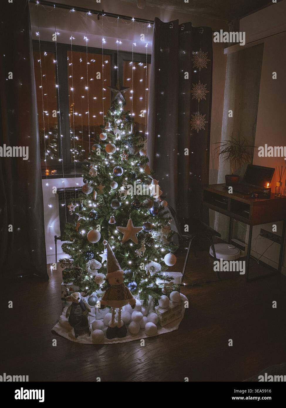 Gemütlicher Weihnachtsbaum, dekoriert mit Lichtern und Ornamenten in einem warmen Wohnraum bei Nacht, festliche Feiertagsatmosphäre. Stockfoto