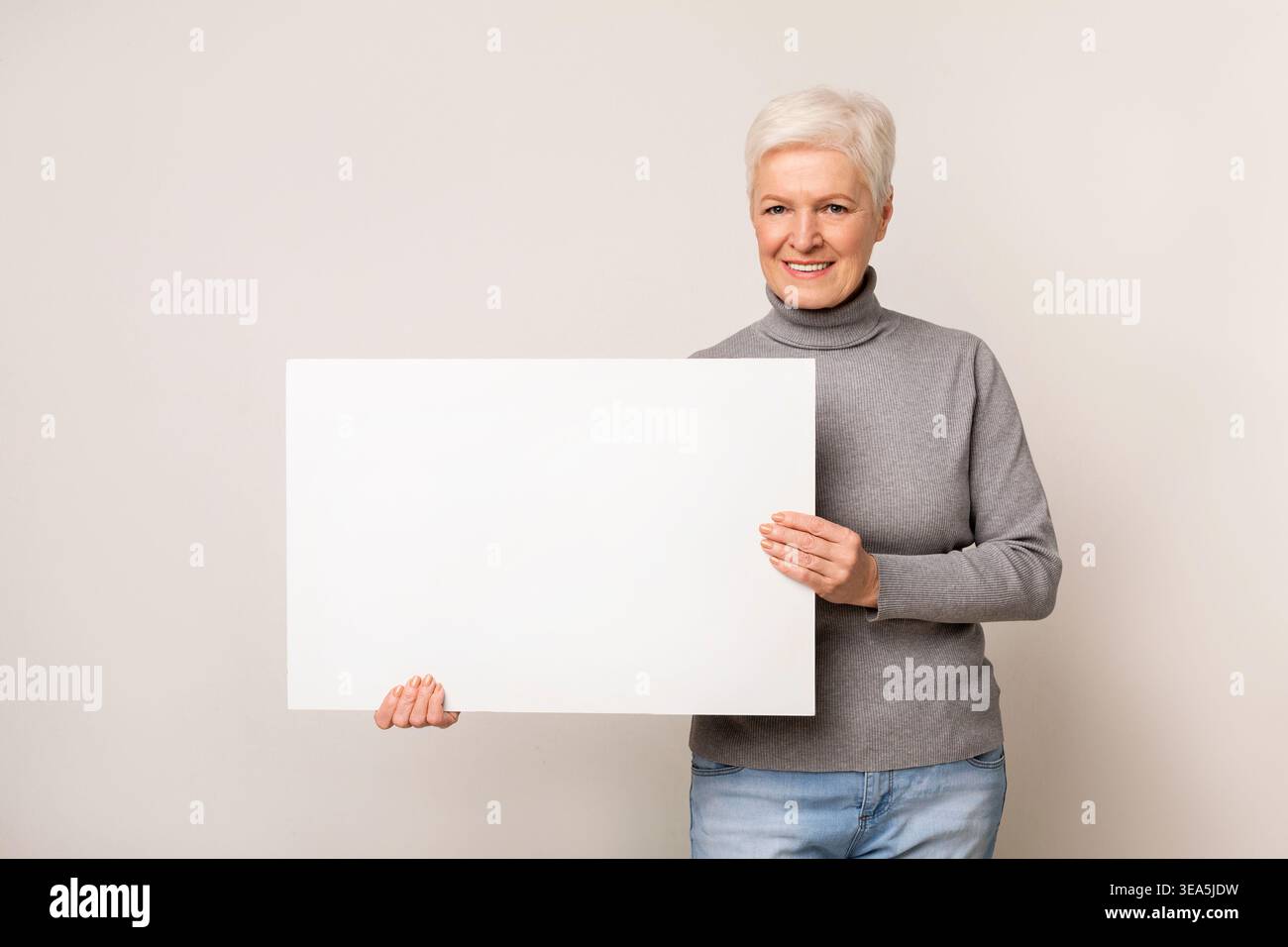 Lächelnde ältere Frau mit leerem Anmelden in ungezwungener Umgebung mit neutralem Hintergrund Stockfoto