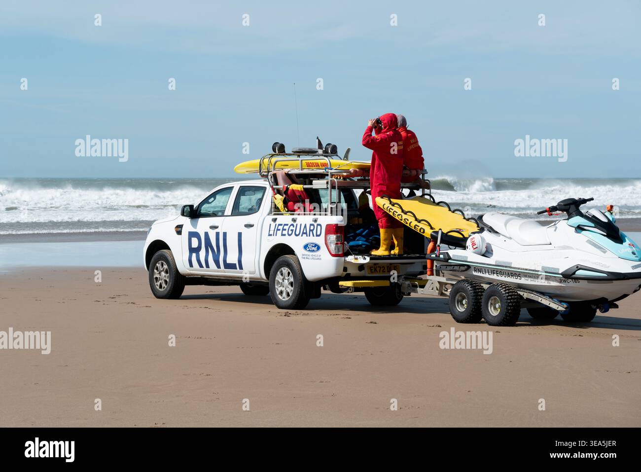 RNLI-Rettungsschwimmer halten in Croyde Bay, Großbritannien, an einem Tag Wache, an dem eine starke Schwingung mit starken Offshore-Winden für anspruchsvolle Surfbedingungen sorgt. Stockfoto