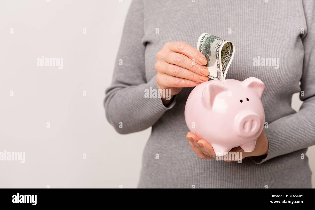 Person spart Geld, indem sie einen Dollar-Schein in eine Sparbank in einer hellen Umgebung legt Stockfoto