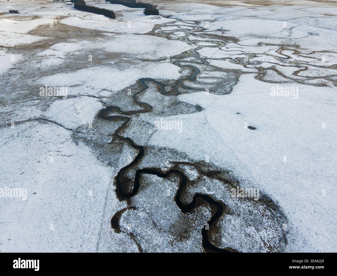 Aus der Vogelperspektive eines sich windenden Flusses, der durch schneebedeckte Felder und ländliche Winterlandschaft in Nasbinals, Occitanie, Frankreich fließt. Stockfoto