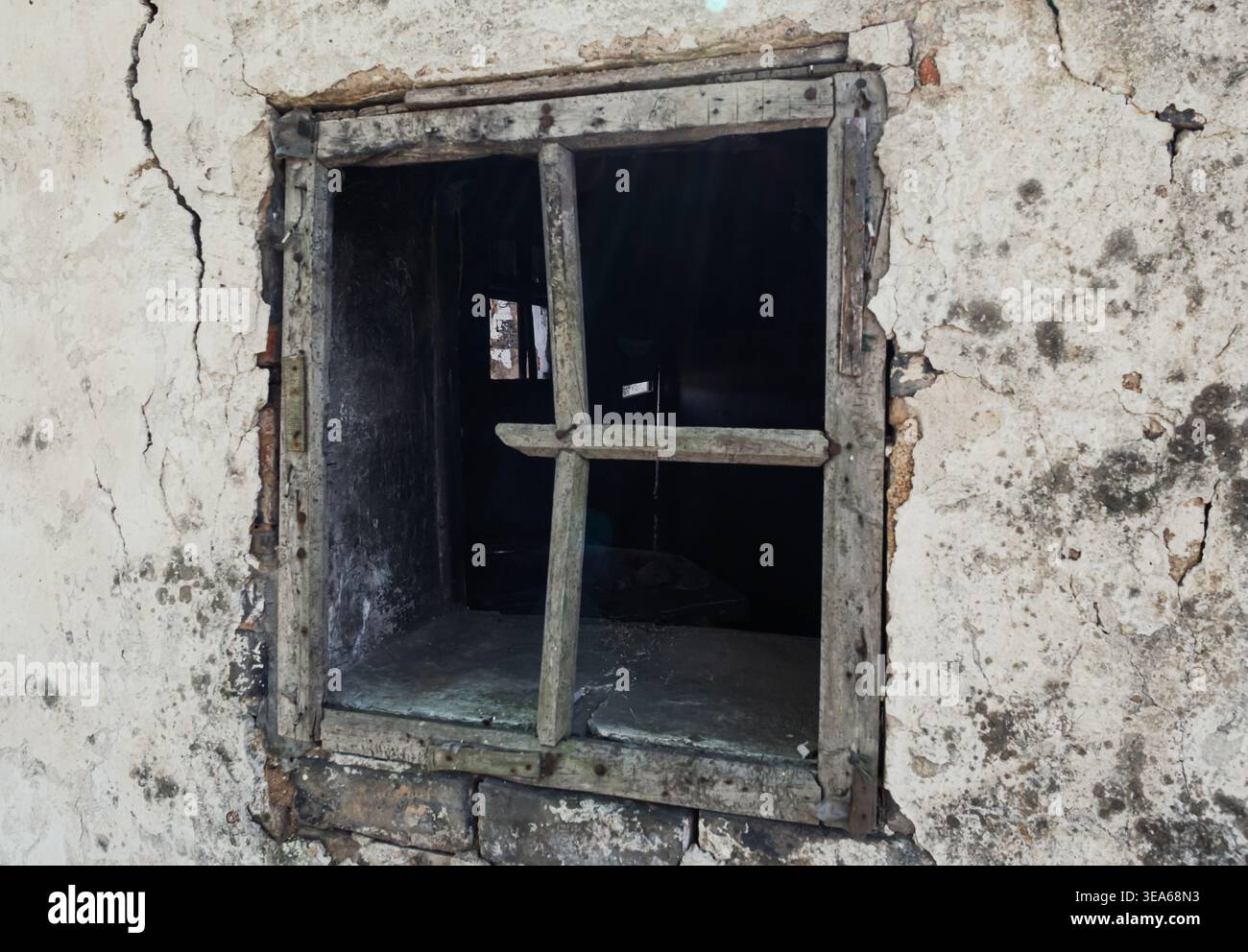 Verfallender Holzfensterrahmen in einer stark gerissenen und verfärbten Wand eines vernachlässigten Gebäudes Stockfoto