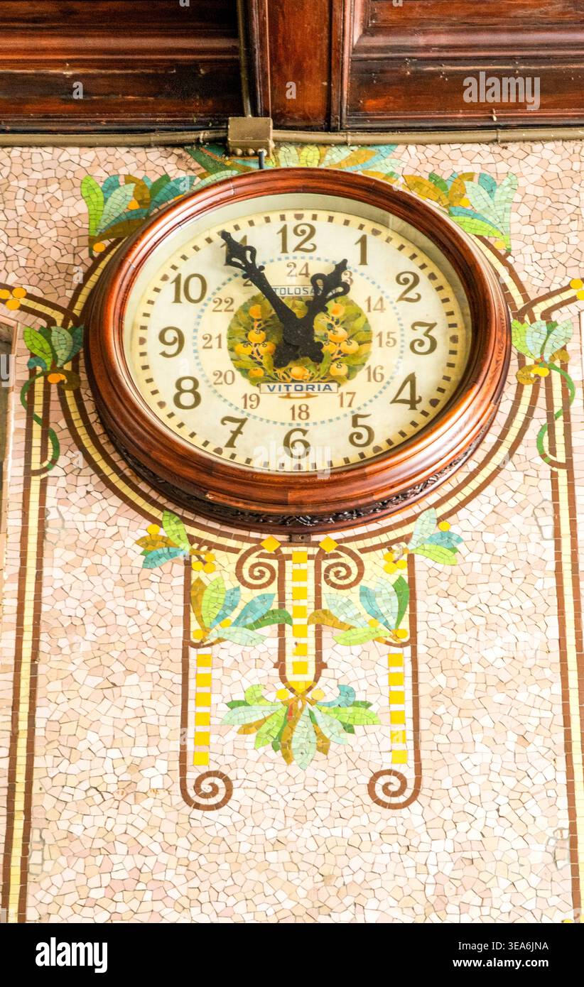 Vintage-Wanduhr mit Holzrahmen an kunstvoll verzierten Mosaikfliesen, Jugendstilgeblümten, warmen Tönen, Inneneinrichtung aus nächster Nähe. Stockfoto