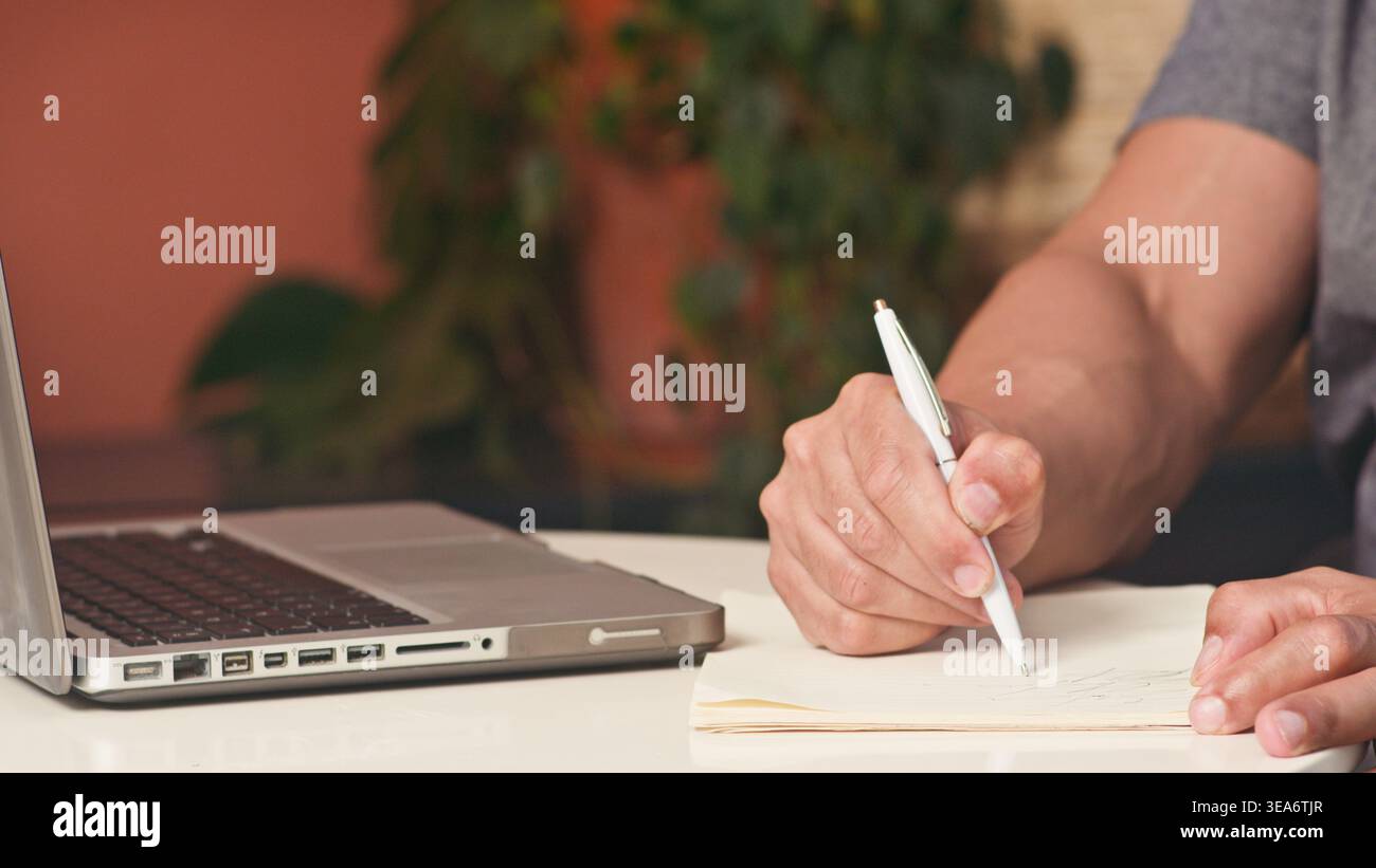 Person, Die Notizen Neben Laptop Im Home Office-Arbeitsbereich Schreibt – Geschäftsplanung Und Produktivität Stockfoto