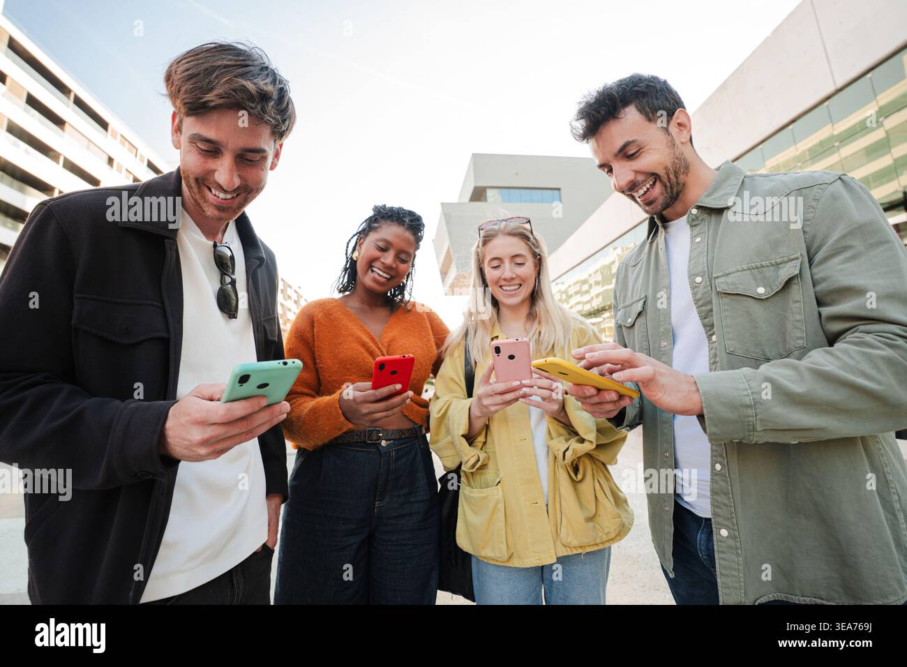 Eine vielfältige Gruppe von Freunden, die gerne mit ihren Smartphones interagieren, fröhliche Momente teilen und lachen, während sie über Technologie und miteinander verbunden sind Stockfoto
