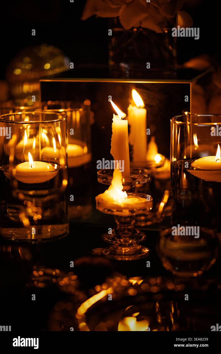 Schwimmende Teelichter und weiße Kerzen in Glashaltern auf dem Tisch Stockfoto