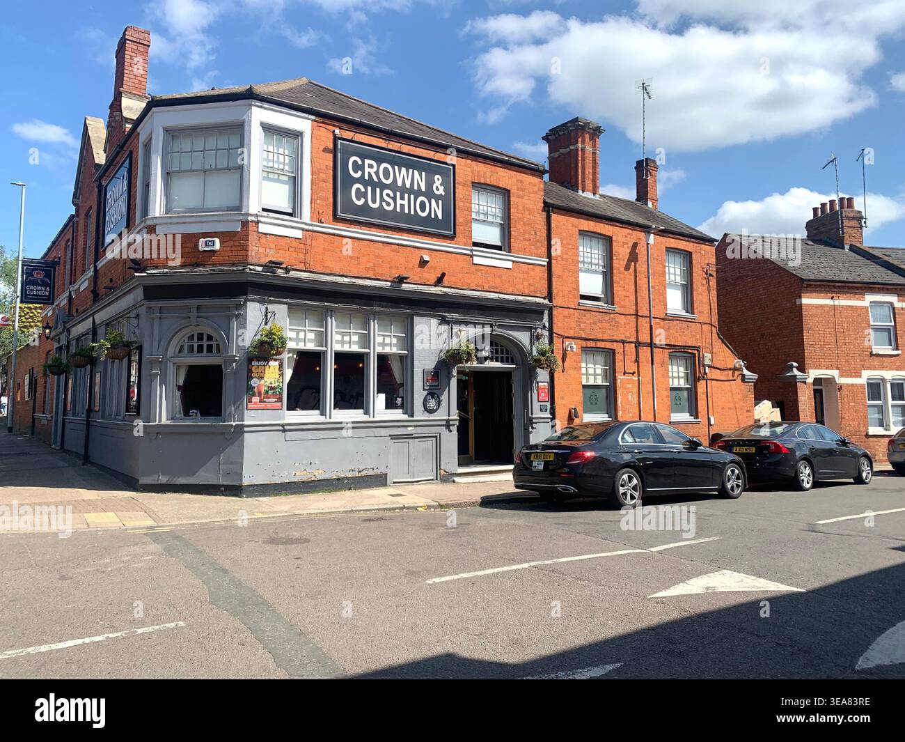 Crown and Cushion Pub an einer sonnigen Straßenecke in einem traditionellen britischen Backsteingebäude in Northampton England, Großbritannien, mit großem Schild - Smartphone-aufgenommenes Stockfoto