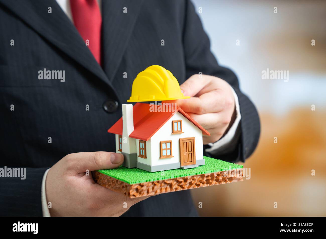Ein Haus mit einem Bauhelm in den Händen eines Geschäftsmannes. Bau, Renovierung und Wiederaufbau bestimmen die Wohnentwicklung. Investition i Stockfoto