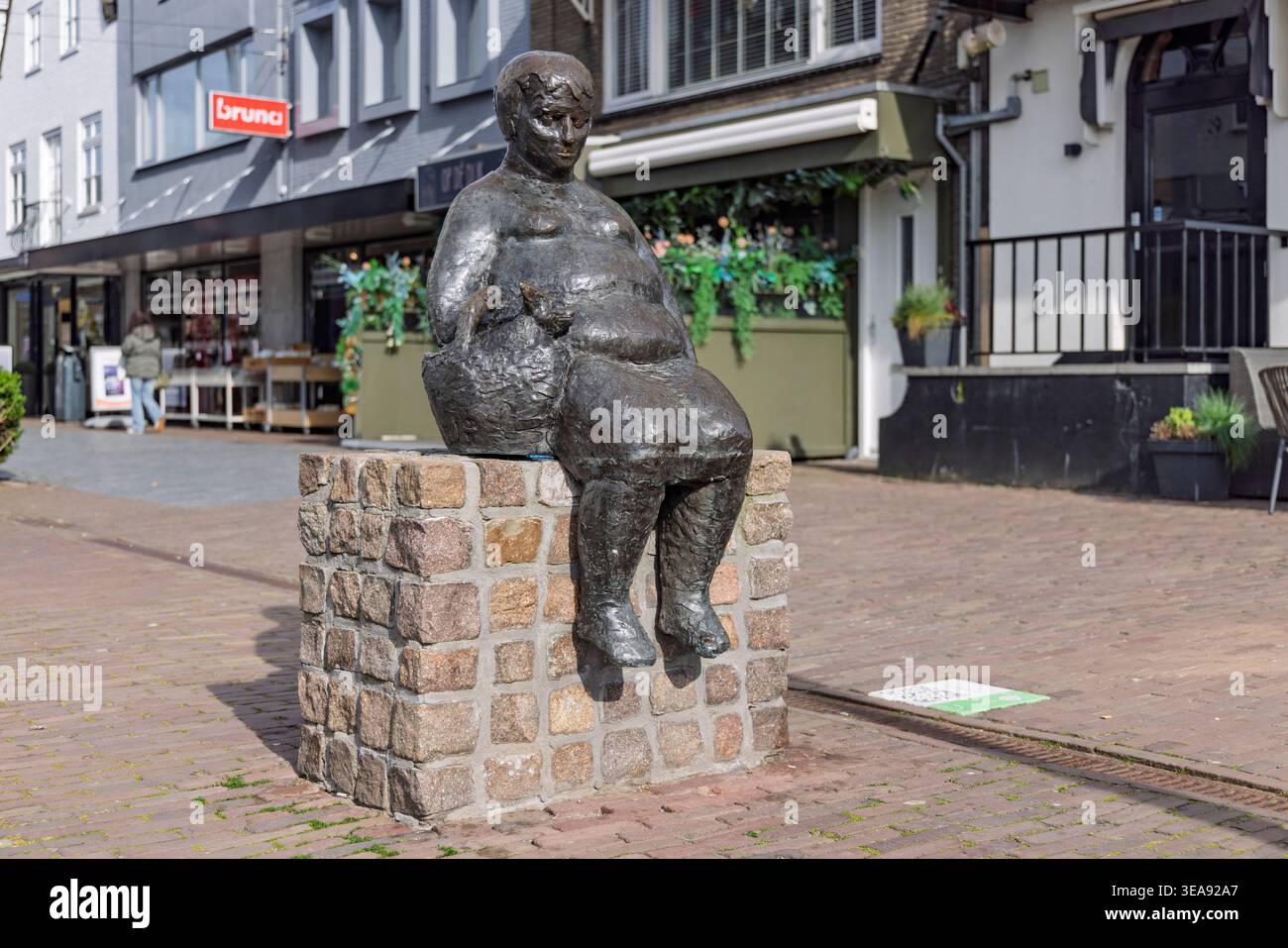 Oud-Beijerland, Niederlande, 15. April 2026. Eine detaillierte Bronzeskulptur einer Frau, die einen kleinen Hund in der Tasche hält, befindet sich in einem Fußgängergeschäft Stockfoto