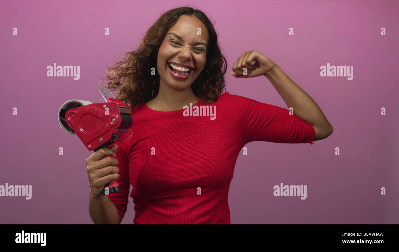Frau mit Klebebandspender und flexiblem Bizeps im Studio mit rosa Hintergrund und breitem lachenden Lächeln; Selbstvertrauen-Feier. Stockfoto