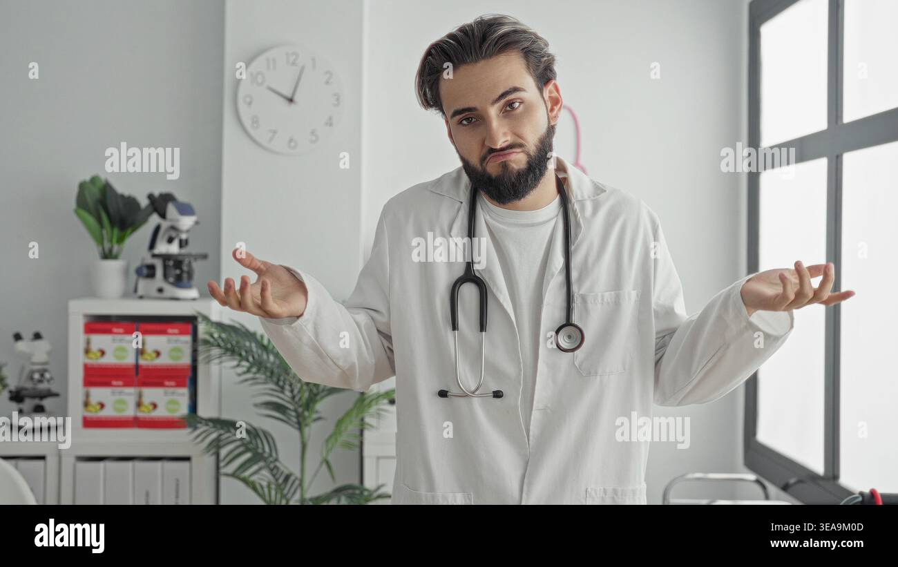 Mann mit Stethoskop zuckt mit Händen in einem weißen Bürogebäude, trägt Labormantel und Bart sichtbar; Unsicherheitsdilemma. Stockfoto