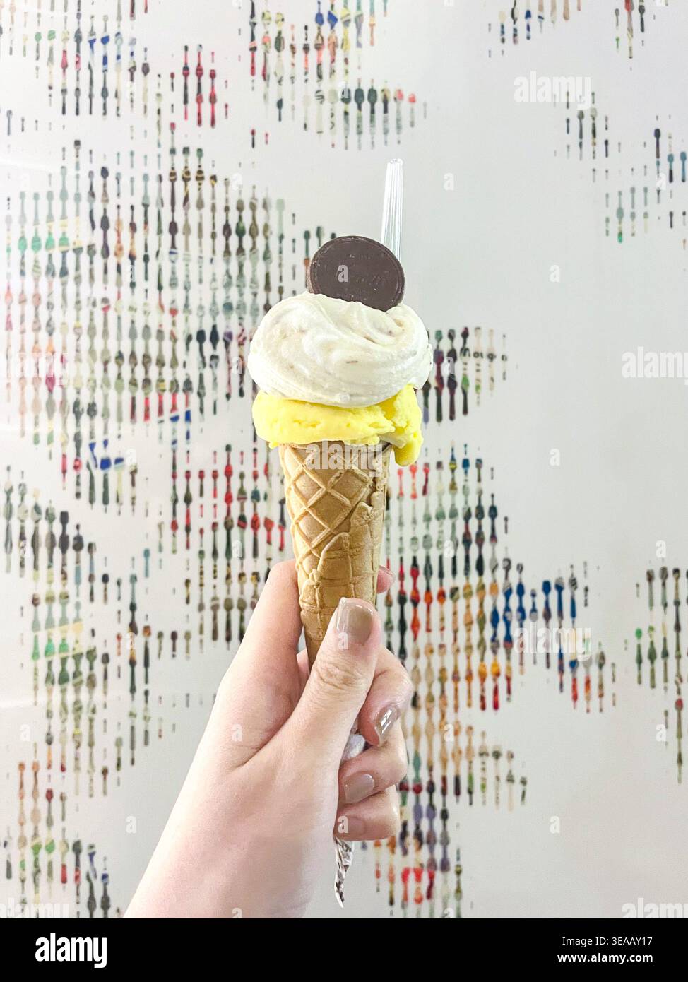 Eine Hand hält ein Waffeleis mit zwei Schaufeln und gelbem und Vanilleweich an einer farbenfrohen Wand in einer japanischen Eisdiele. Stockfoto