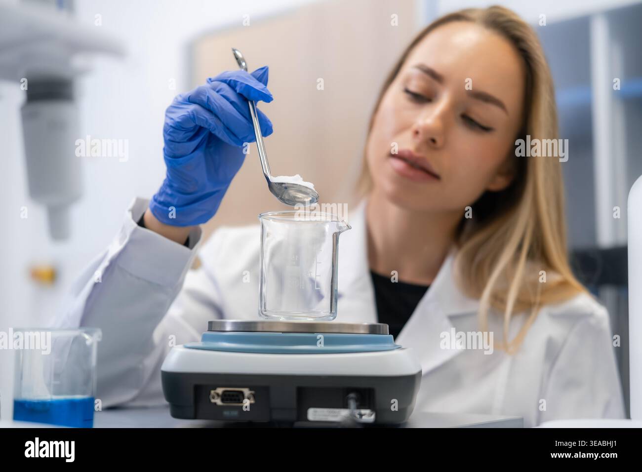 Labortechniker wiegen mit einem Löffel über einem Glasbecher auf Waagwaage präzise Mengen des Chemiepulvers ab. Stockfoto
