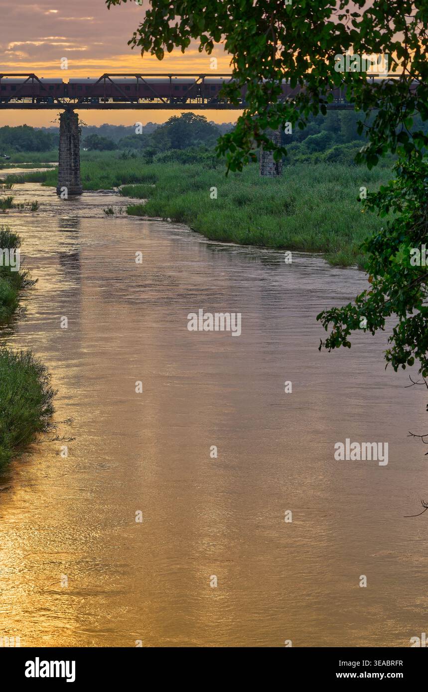 Sonnenaufgang auf dem Sabie River vom Skukuza Rastlager mit der historischen Eisenbahnbrücke und Zugwagen, Kruger Nationalpark, Südafrika Stockfoto