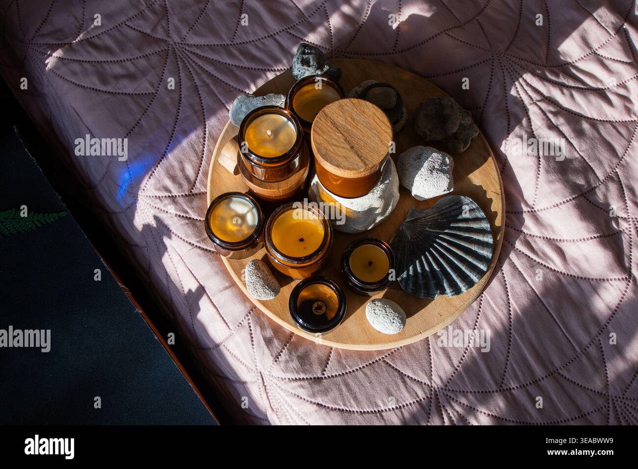 Anordnung von Kerzen und Steinen auf dem Tablett. Bernsteingläser mit Holzdeckeln auf dem Bett. Kerzenglas und Flaschen mit Natural Elements Draufsicht zu Hause. Stockfoto