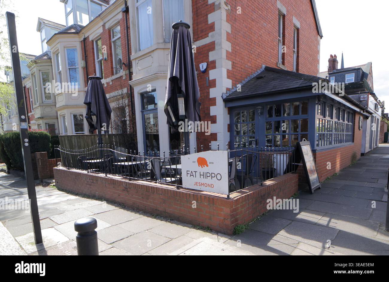 FAT Hippo liegt auf der St Georges Terrace in Jesmond, einem exklusiven Vorort von Newcastle upon Tyne. Am 15. April 2026 zeigt der Bereich Sitzplätze im Freien mit Tischen und Sonnenschirmen für Gäste. Das Restaurant hat ein Schild auf der Vorderseite mit seinem Namen. Die Gebäude in der Nähe sind klassisch gestaltet und tragen zum Charme der Nachbarschaft bei. Stockfoto