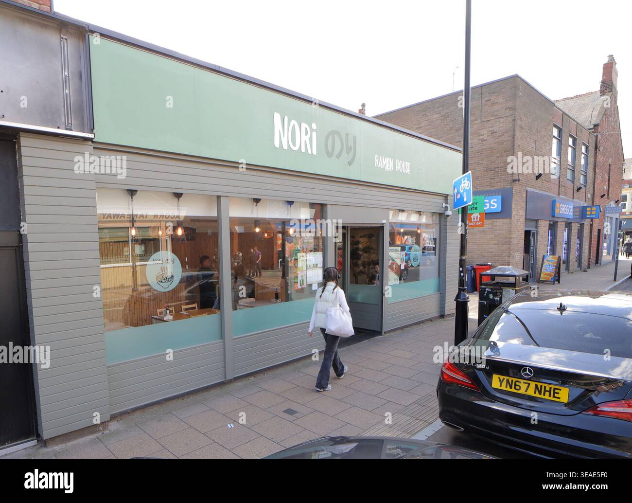 Am 15. April 2026 läuft eine Person in Richtung Nori Ramen, die sich an der Acorn Road in Jesmond, Newcastle upon Tyne befindet. Das Restaurant hat ein sauberes und einfaches Design. Mehrere Geschäfte nebenan sind zu sehen, was zur lebhaften Atmosphäre der Gegend beiträgt. Die Sonne scheint auf der Straße und verleiht diesem Teil von Jesmond eine lebendige Atmosphäre. Stockfoto