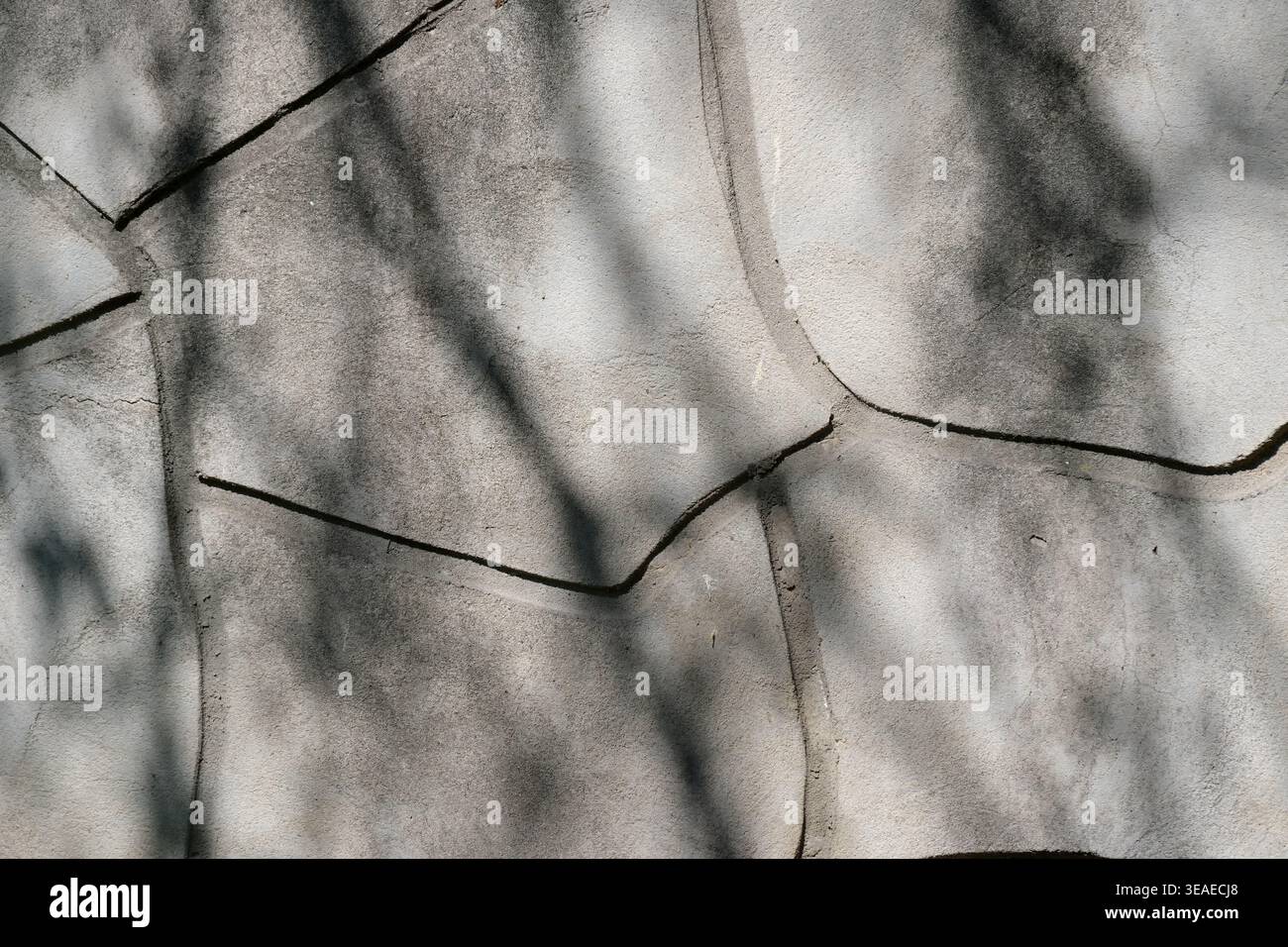 Das Licht tanzt über einer strukturierten Wand und offenbart einzigartige Formen und Schatten auf spielerische Weise. Stockfoto