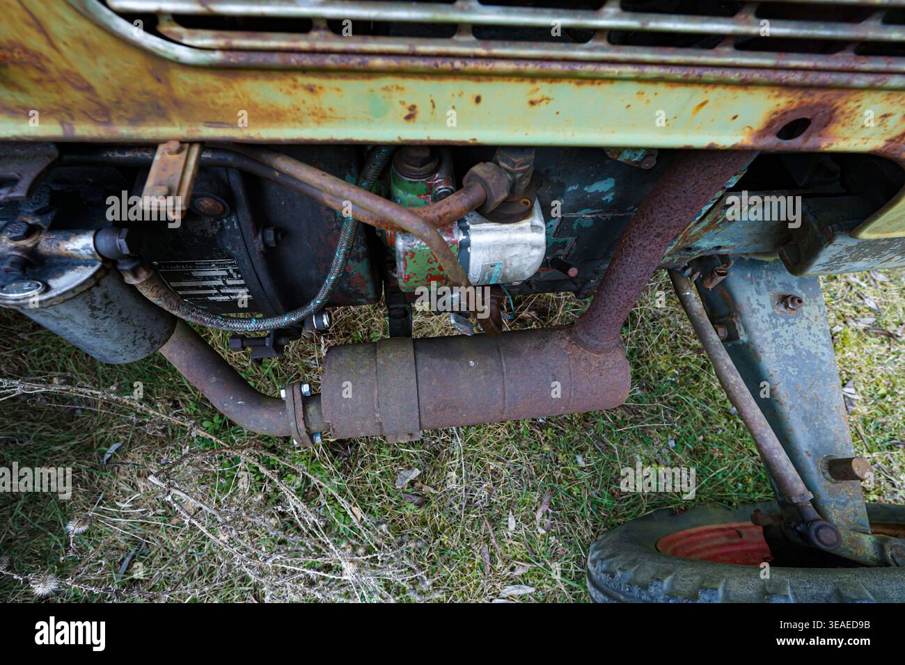 Verrostete Traktormotorkomponenten und Auspuffanlage, die auf einer alten Landmaschine im Freien auf einem Grasfeld abgestellt sind. Stockfoto