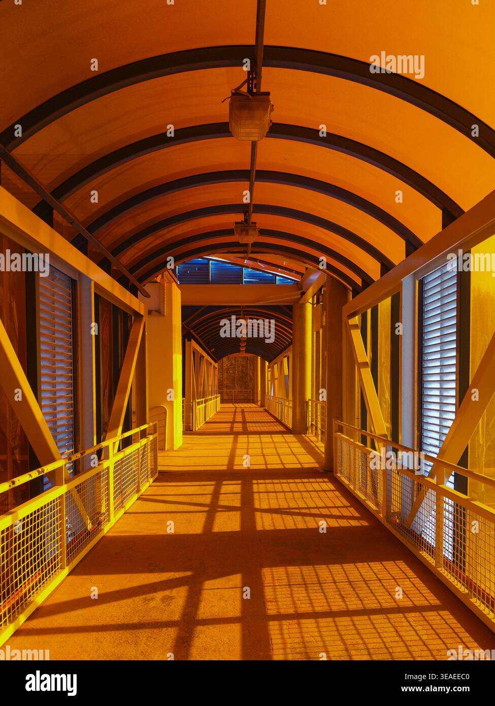 Perspektivische Ansicht eines perfekt symmetrischen Tunnels, beleuchtet mit leuchtendem orangefarbenem Licht, schafft eine filmische und futuristische urbane Atmosphäre. Stockfoto