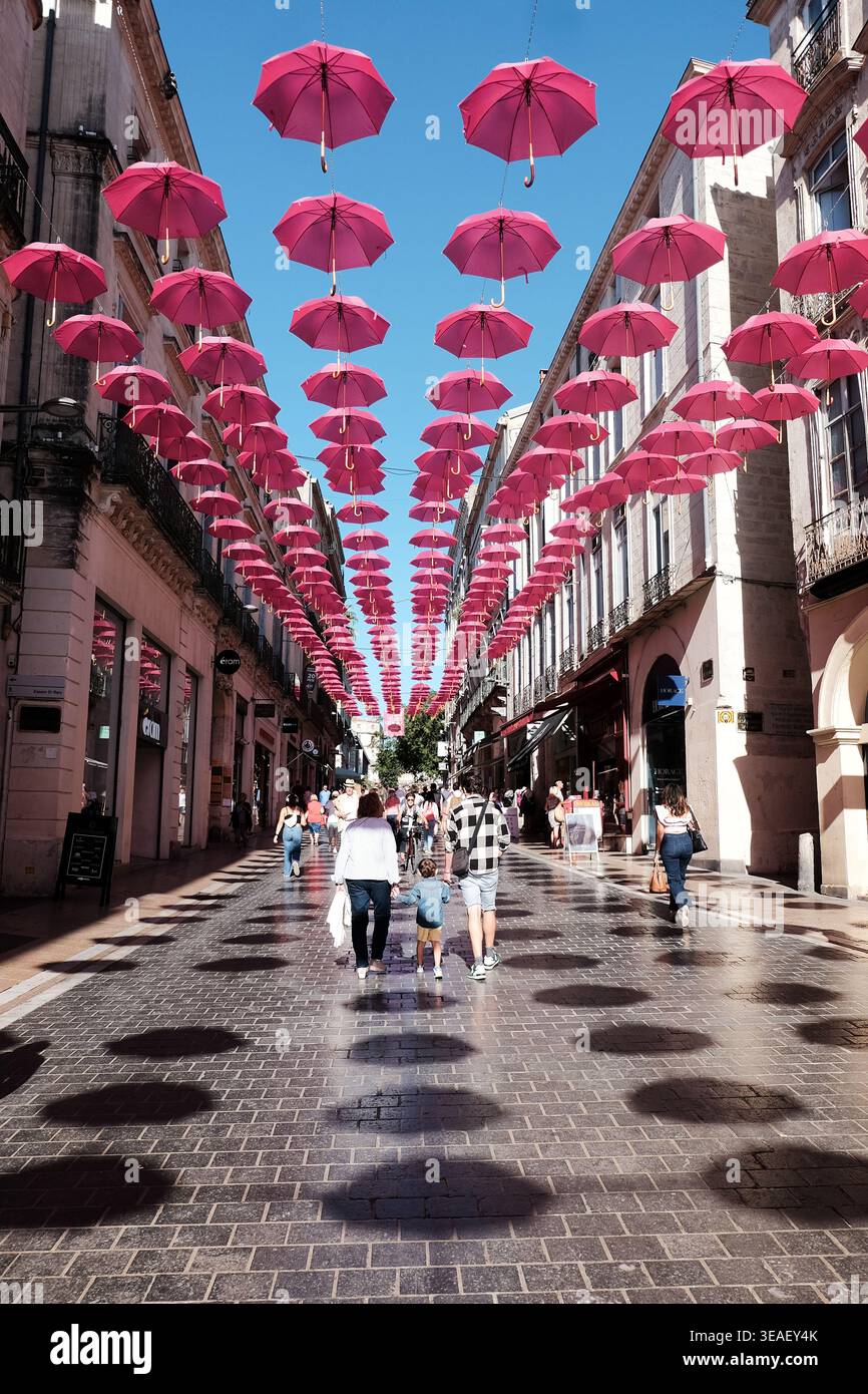 Fußgängerzone mit pinkfarbenen Sonnenschirmen unter einem hellblauen Himmel im Stadtzentrum von Montpellier, Frankreich. Stockfoto