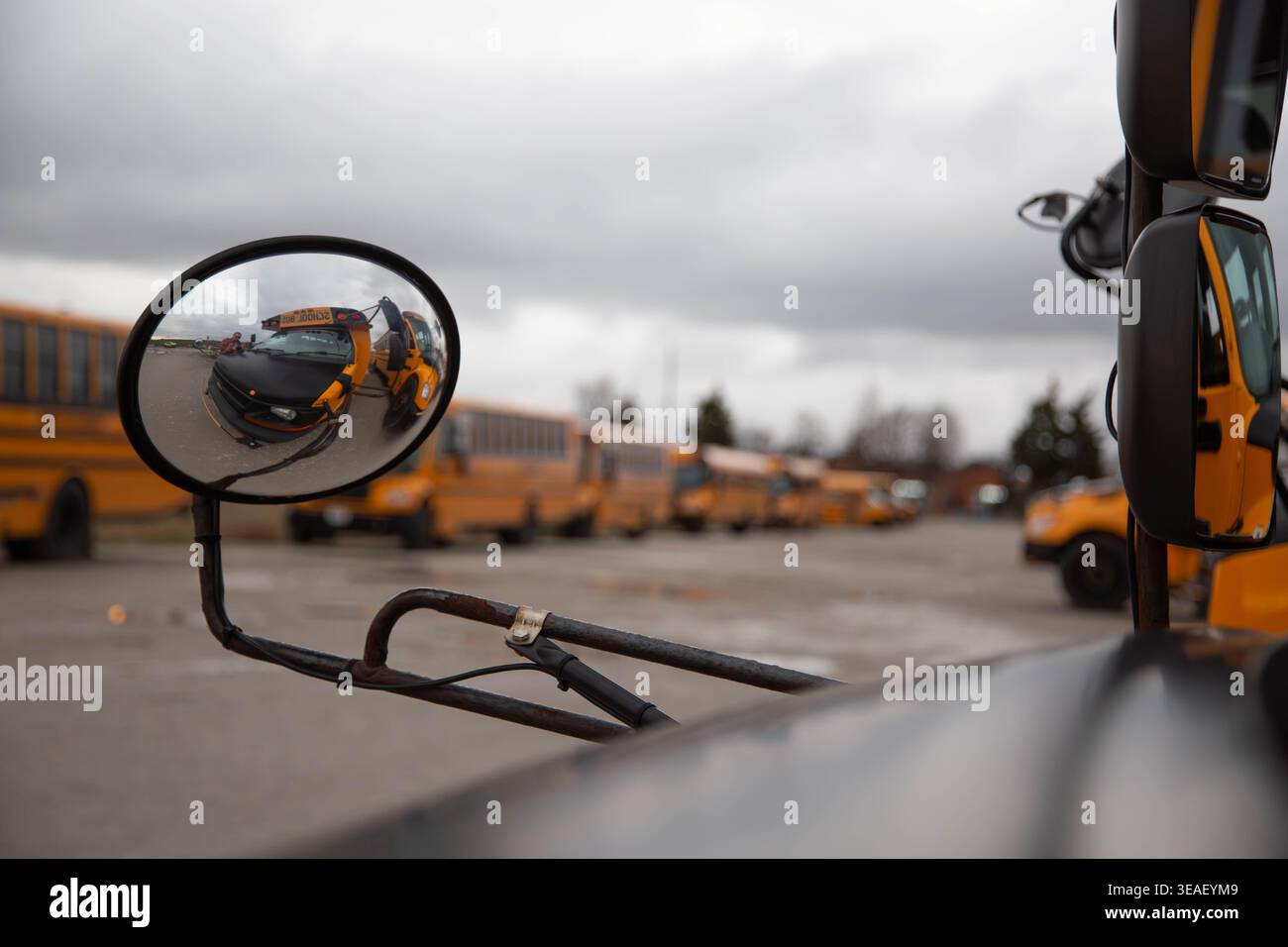 Nahaufnahme eines Seitenspiegels eines Schulbusses, der eine Reihe gelber Busse in einem Depot mit geringer Schärfentiefe reflektiert. Stockfoto