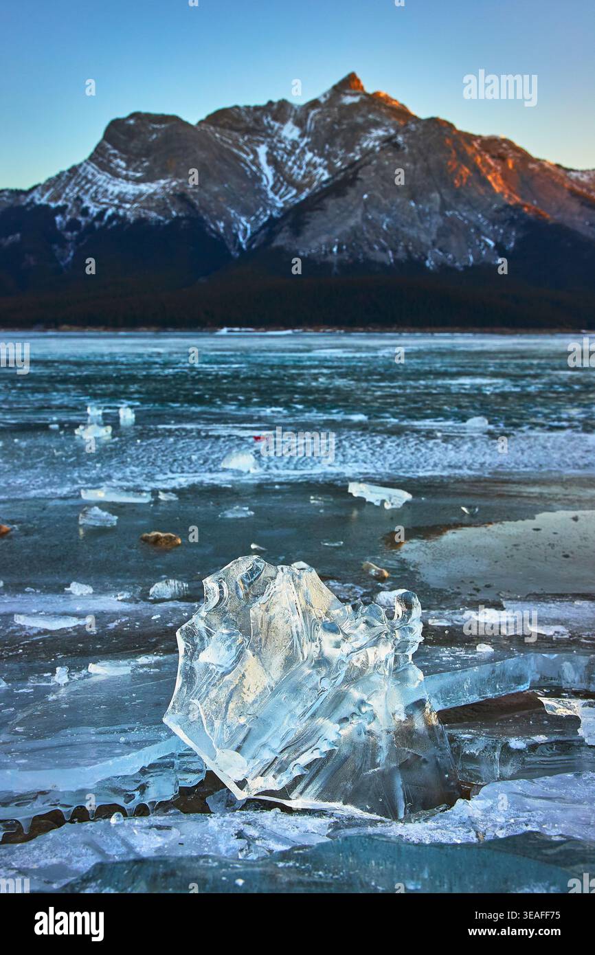 Eisfragment auf dem gefrorenen See und schneebedeckter Berg bei Wintersonngang Stockfoto