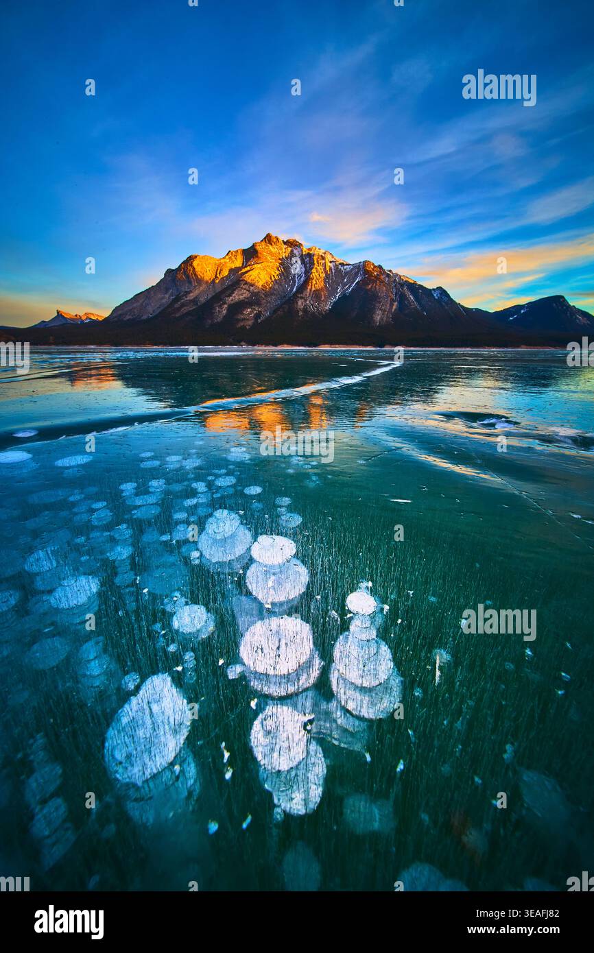 Gefrorene Methanblasen und schneebedeckte Berge spiegeln sich auf der Oberfläche des Winter Lake Stockfoto