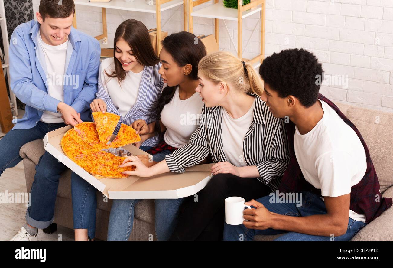 Freunde genießen gemeinsam Pizza in einem gemütlichen Wohnzimmer an einem Wochenendabend Stockfoto
