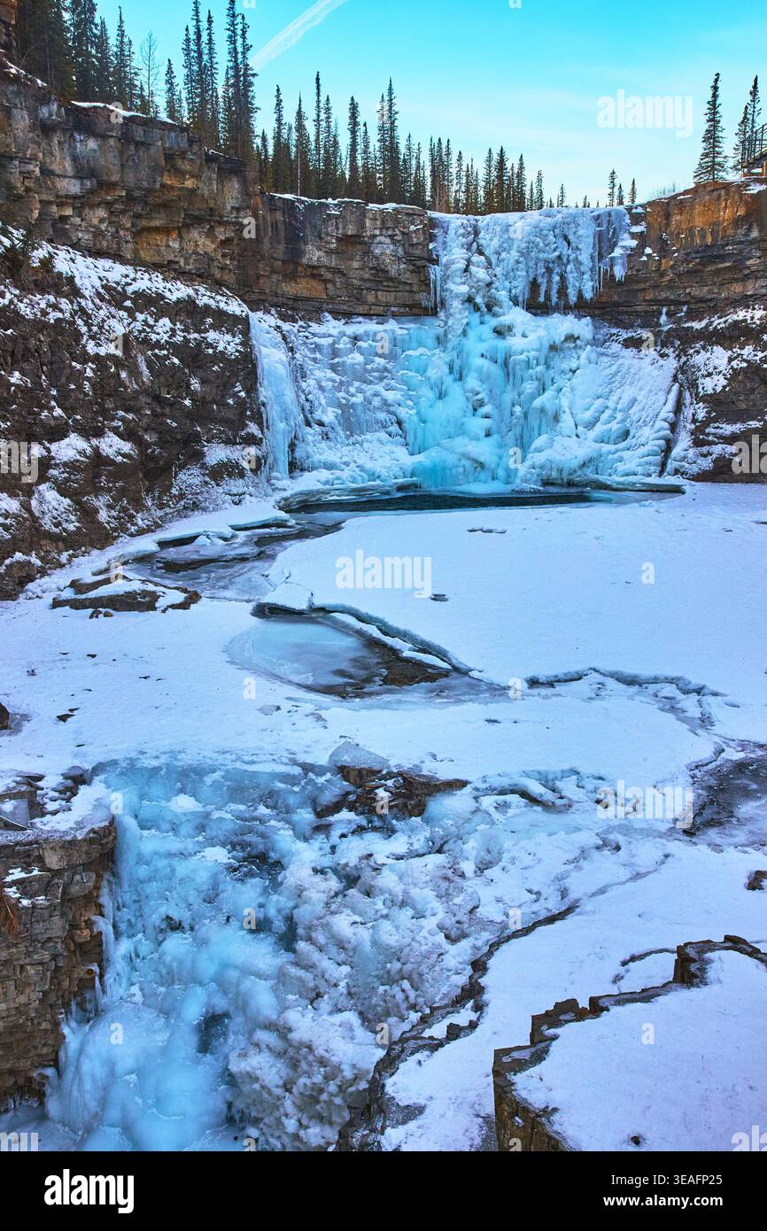 Gefrorener Wasserfall und schneebedeckter Canyon mit immergrünen Bäumen im Winter Stockfoto