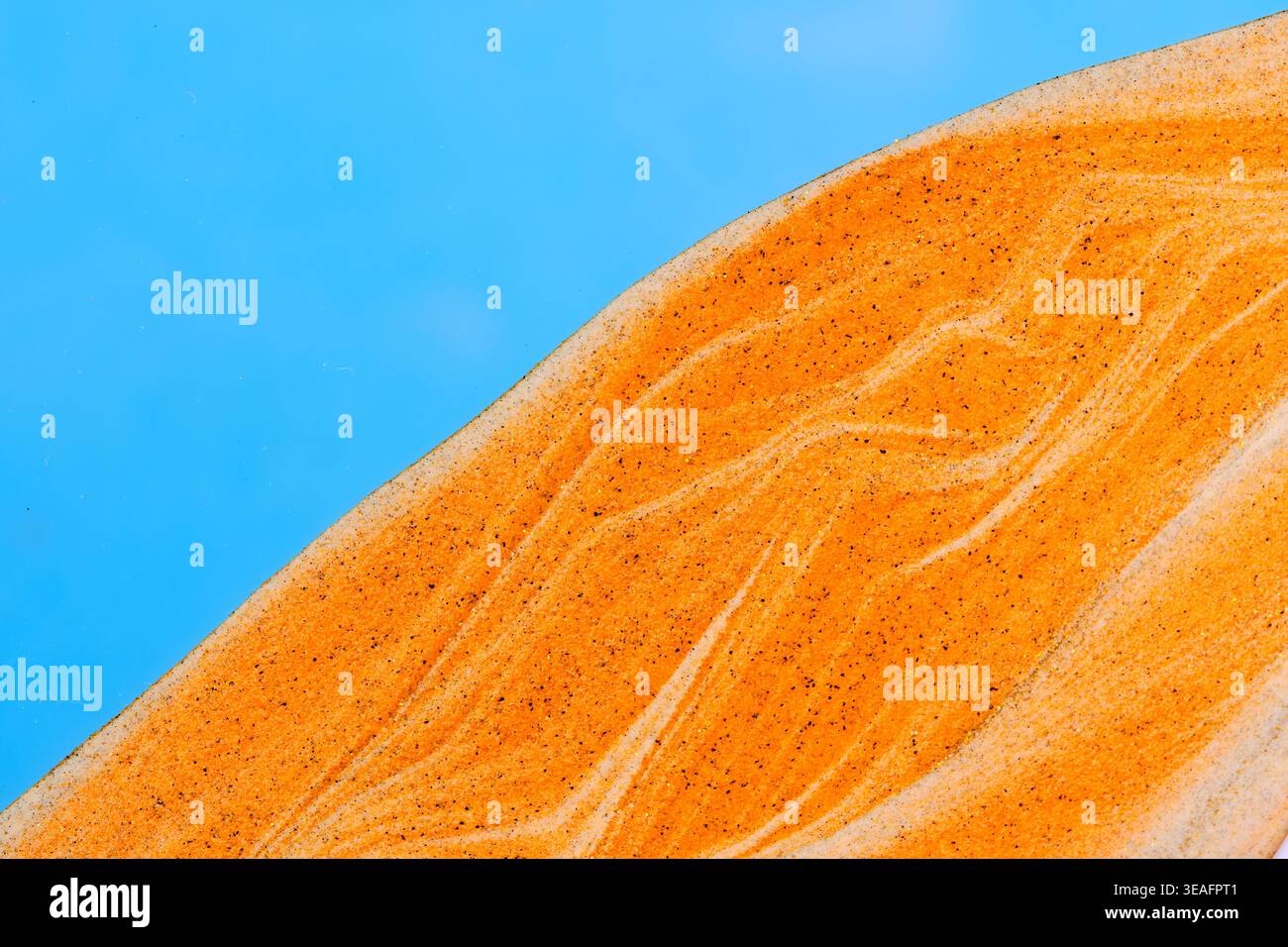 Leuchtend orange Sandstrukturen schaffen organische Wellenmuster mit goldenem Glitzer und feinen Körnern Stockfoto