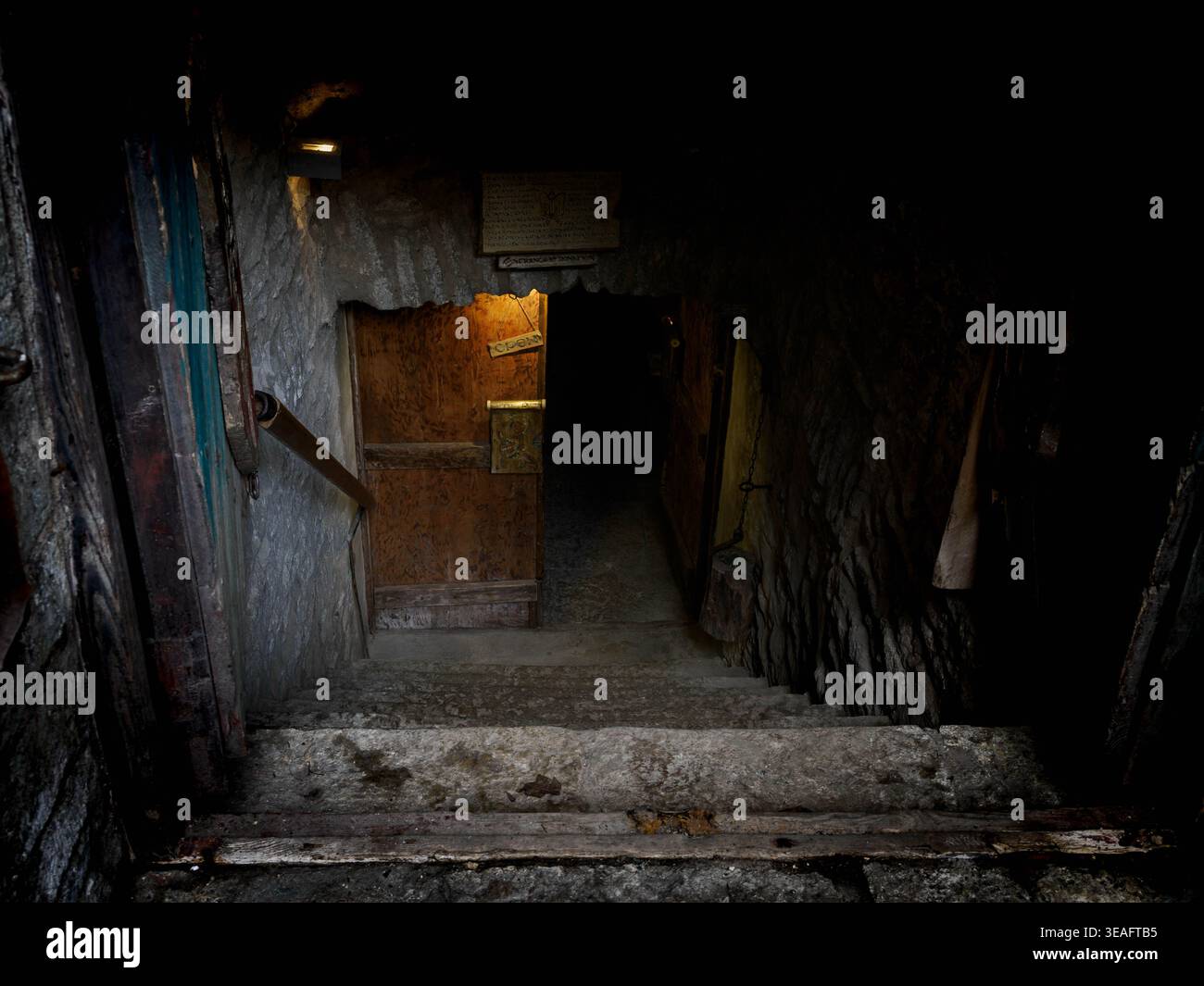 Dunkle Steintreppe führt zu einer Kellertür in der Altstadt von Tallinn, Estland, mit warmem Licht und Kalksteinwänden Stockfoto