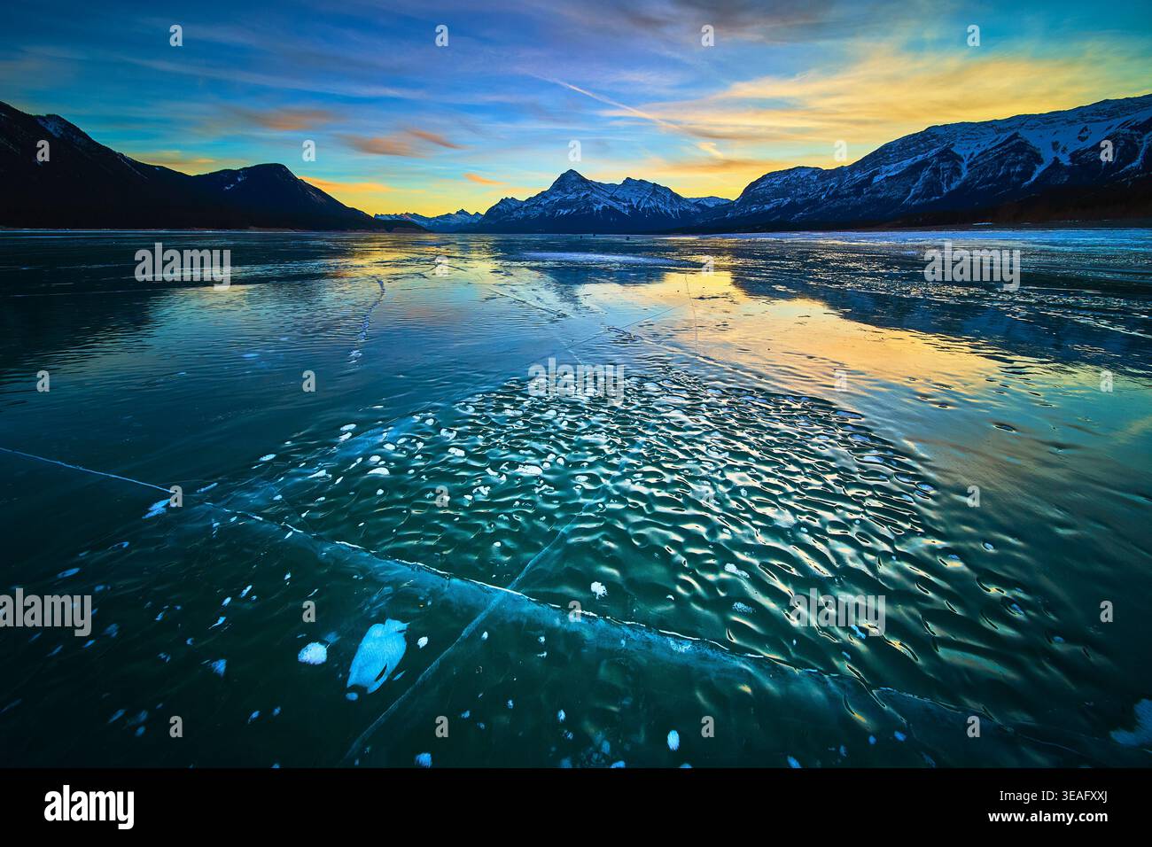 Frozen Lake Ice Patterns und schneebedeckte Berge bei lebendigem Winteruntergang Stockfoto