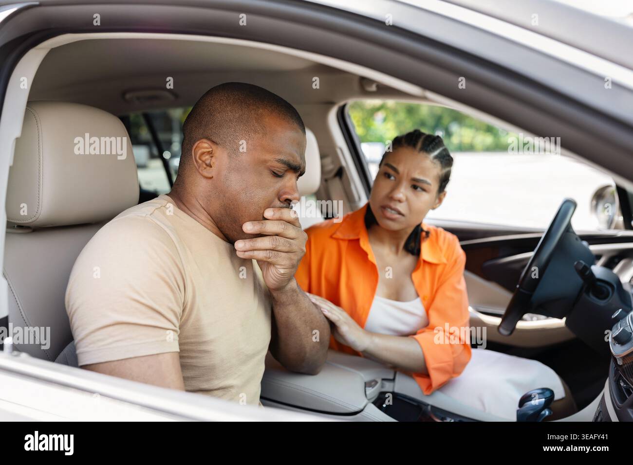 Junger Schwarzer, der sich krank fühlt und den Mund mit der Hand im Auto bedeckt Stockfoto