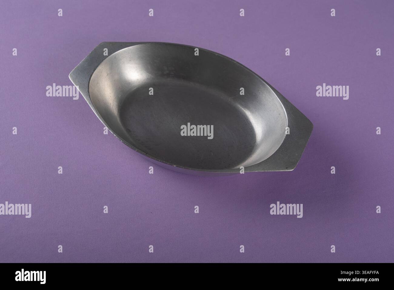 Die Nahaufnahme zeigt eine Servierschale aus Metall, isoliert auf violettem Hintergrund. Studio-Beleuchtung, neutrale Töne, gebürstetes Metall. Vermittelt Einfachheit, Küchenzeile Stockfoto