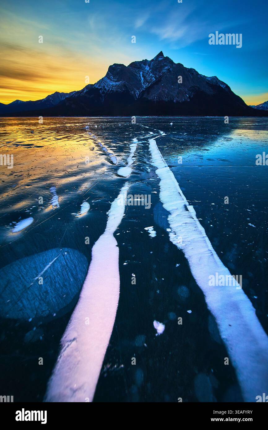 Frozen Lake Risse und Schneeflächen bei Sonnenaufgang mit Mountain Silhouette Winter Stockfoto