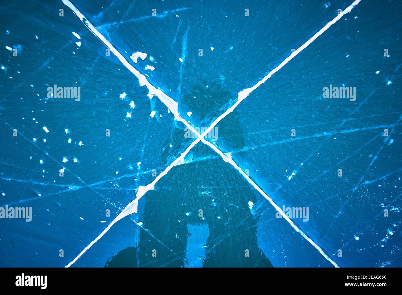 Cracked Ice Pattern auf gefrorenem See mit tiefblauen Winterreflexionen Stockfoto