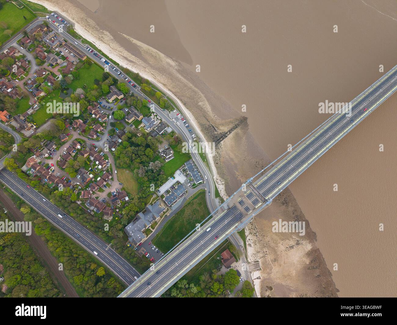 Aus der Vogelperspektive auf die Humber Bridge, die das schlammige Wasser der Humber Mündung überquert, neben Wohnhäusern und grünen Gärten in Kingston upon Hull, E Stockfoto