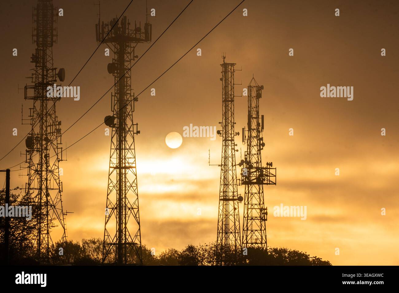 Telekommunikationstürme und Mobiltelefonmasten, die sich vor einem strahlenden Sonnenuntergangshimmel mit sichtbaren Antennen und Sendeanlagen darstellen Stockfoto